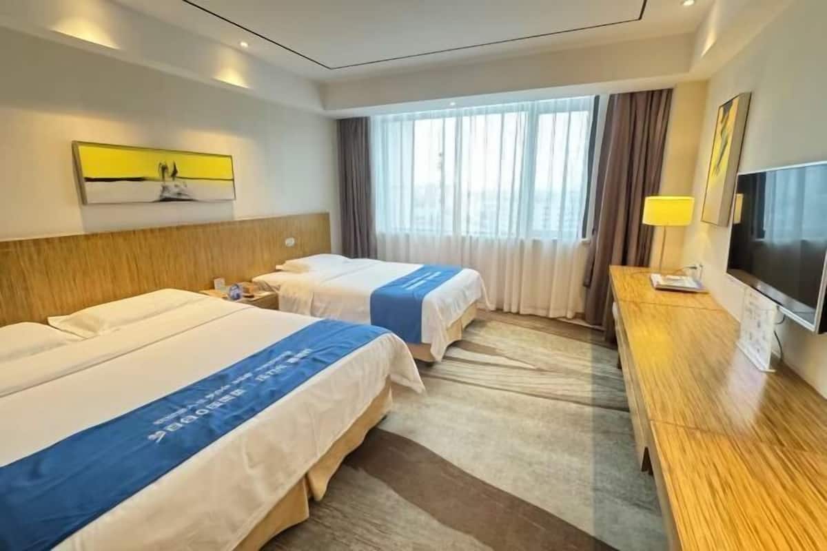 A hotel room with two beds, a wooden desk, a TV, and a window with curtains.