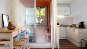 A compact kitchen with white cabinets, a dining area with a wooden table and chairs, and a sliding glass door leading to a balcony. - Les Marquises by Interhome (La Grande Motte)