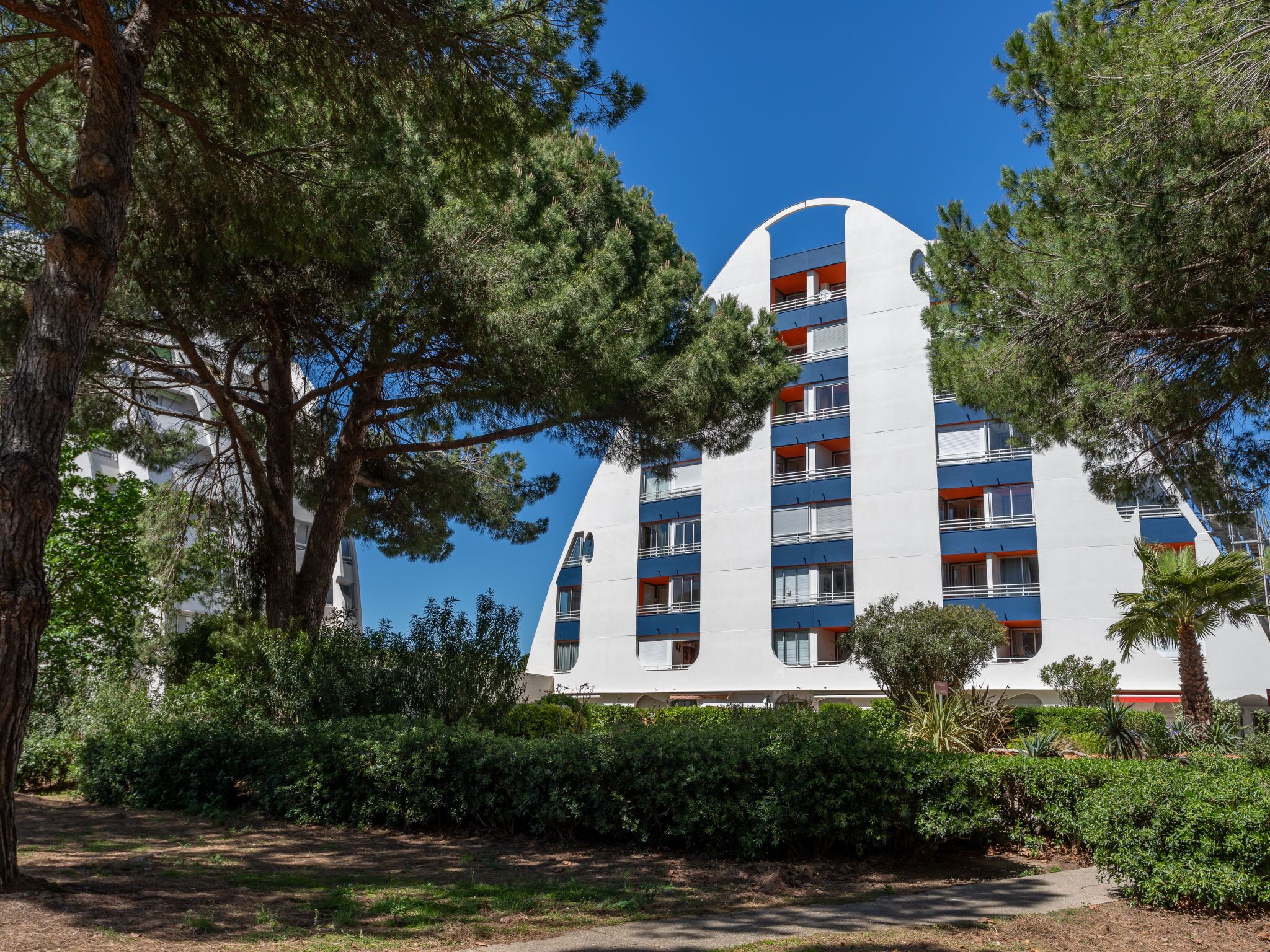 Un bâtiment moderne doté d’une façade incurvée originale, entouré d’une végétation luxuriante et d’arbres.