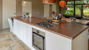 Cocina moderna con isla central, horno integrado y comedor con televisor.