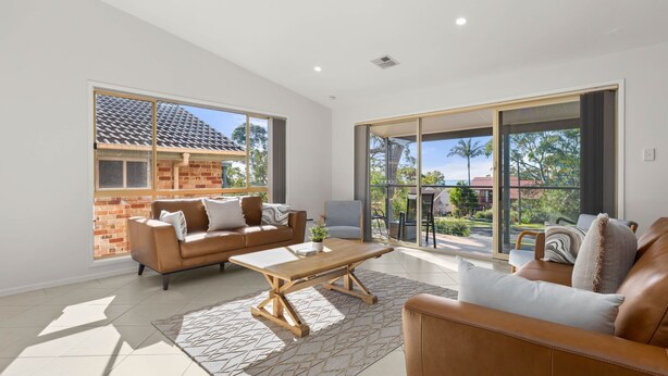 A spacious living room with a brown leather sofa, a wooden coffee table, and a large sliding glass door leading to a balcony.