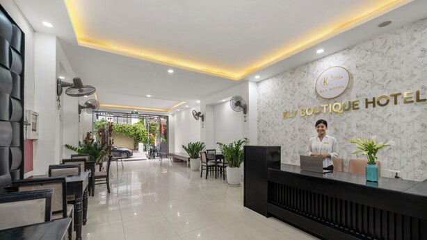 Uma área de recepção de hotel com design moderno, apresentando um balcão de recepção, espaço de estar e um letreiro fixado na parede para o Kly Boutique Hotel.