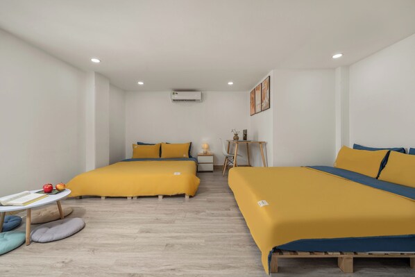 Una habitación de hotel moderna con dos camas, una mesita pequeña con libros y manzanas, una silla y una mesita de noche con una lámpara.