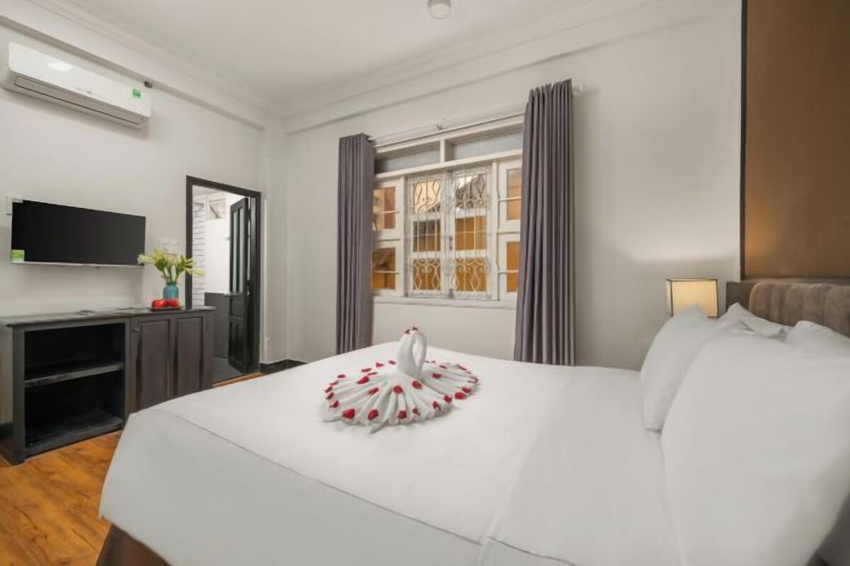 A hotel room with a bed, a flat-screen TV, a desk with a computer, and a window with curtains.