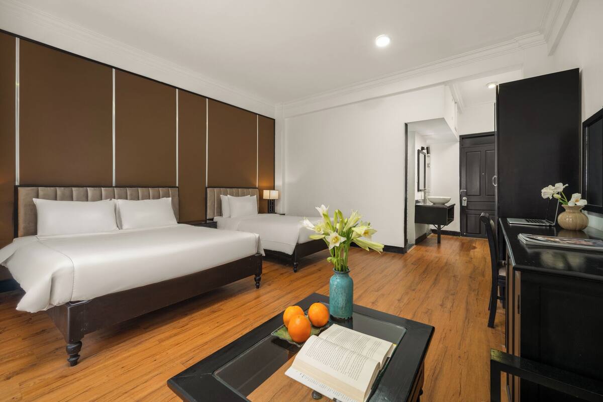 A hotel room with two beds, a dining table with a vase of flowers, and a laptop on the table.