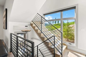 A modern staircase with a glass railing, leading to a balcony with a view of greenery and hills. - Frostwood Retreat | Hot Tub & Shuttle to Gondola (Park City)