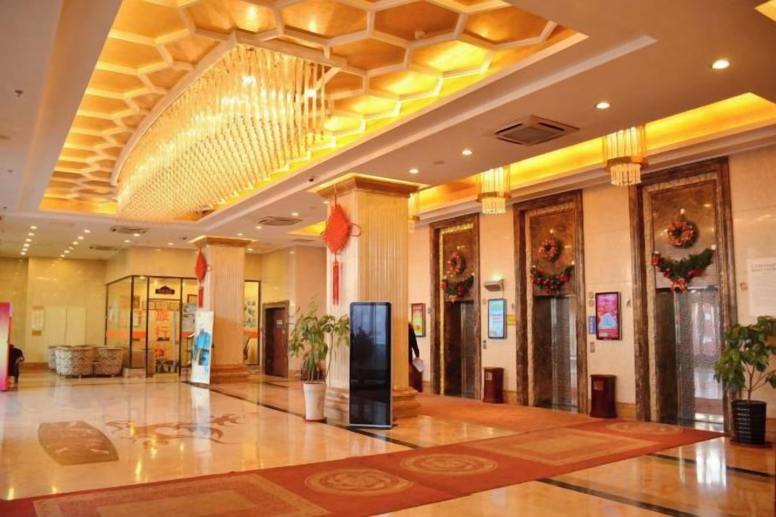 Un vestíbulo de hotel con una araña central, un mostrador de recepción y una alfombra roja grande.