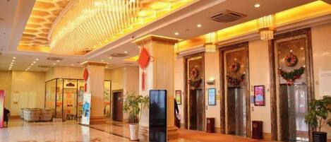 A hotel lobby with a central chandelier, a reception desk, and a large red carpet.