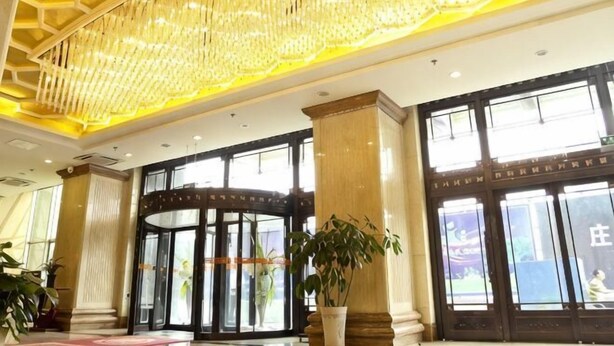 Un vestíbulo de hotel con una lámpara de araña imponente, ventanas amplias y puerta giratoria.