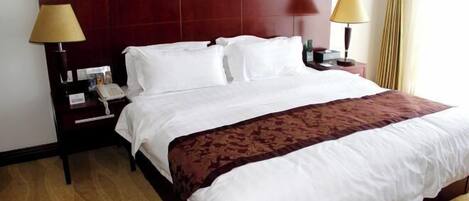 A hotel room with a large bed, two bedside lamps, a telephone, and a nightstand.
