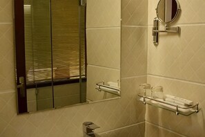 Un baño con un espejo, un perchero para toallas y un estante de vidrio.