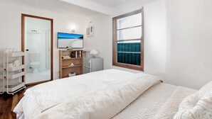 A bedroom with a bed, a TV, a desk, a chair, a wardrobe, and a window.