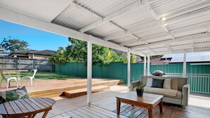 A covered patio with wooden flooring, a sofa, a table, and chairs.