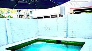 A swimming pool with a blue umbrella, surrounded by a white wall and a tiled deck.