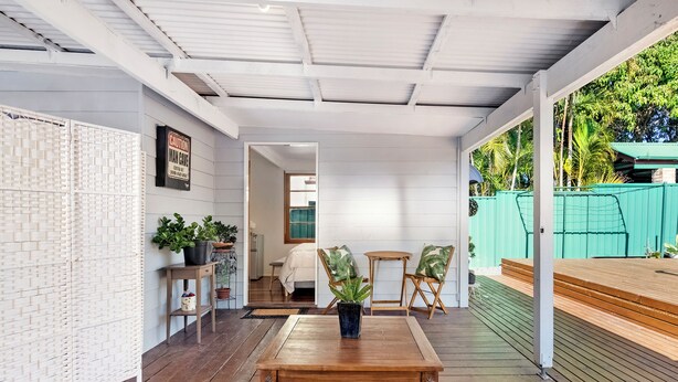A covered patio area with a wooden table and chairs, potted plants, and a view of the interior through a doorway.