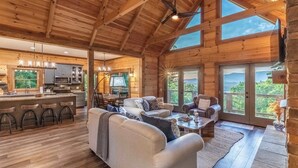 A spacious wooden cabin interior with a living area, kitchen, and large windows offering views of the outdoors. - Luxury Cabin: Lake view/access, Theater, Game room (Bryson City)