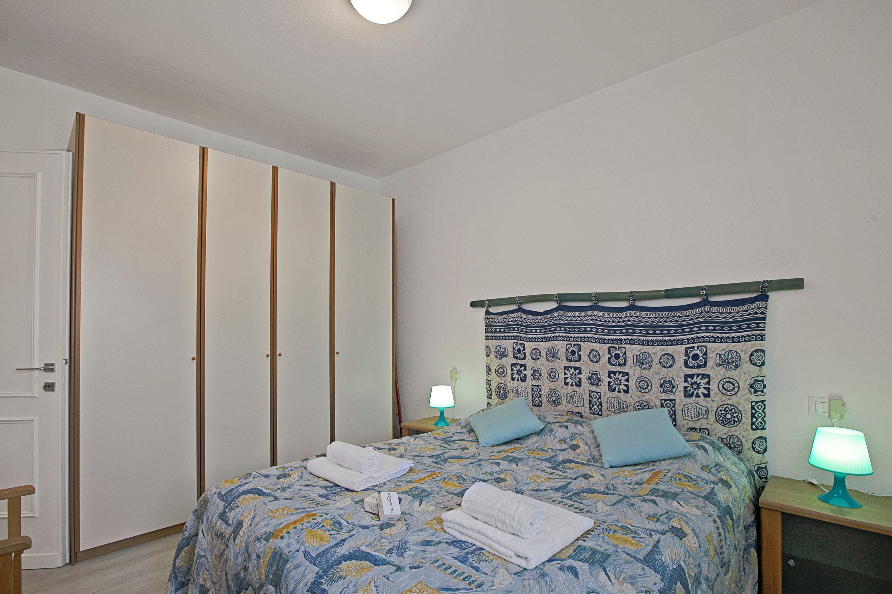 Un dormitorio con una cama, dos lámparas de noche, un cabecero estampado y un armario.
