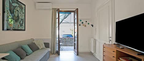 Un salon avec un canapé, un téléviseur et une porte donnant sur l’extérieur.