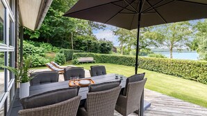 An outdoor patio with a table and chairs, a large umbrella, and a view of a lake and greenery. - Awesome home in Ry with WiFi (Ry)