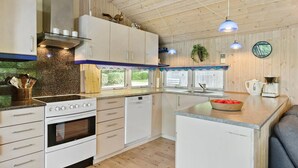 A modern kitchen with white cabinets, a built-in oven, a sink, and a coffee maker. There are wooden beams on the ceiling and a window with a view of greenery outside. - Awesome home in Ry with WiFi (Ry)