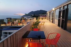 A wooden deck with outdoor seating, overlooking a body of water and a mountain.