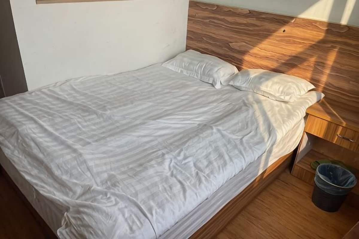 A single bed with a wooden headboard, a white bedspread, and a small trash bin beside it.