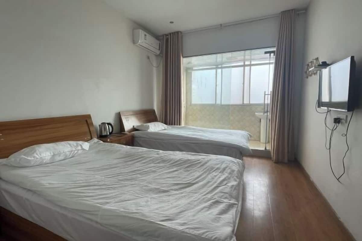 A hotel room with two beds, a TV, an air conditioner, and a balcony with curtains.