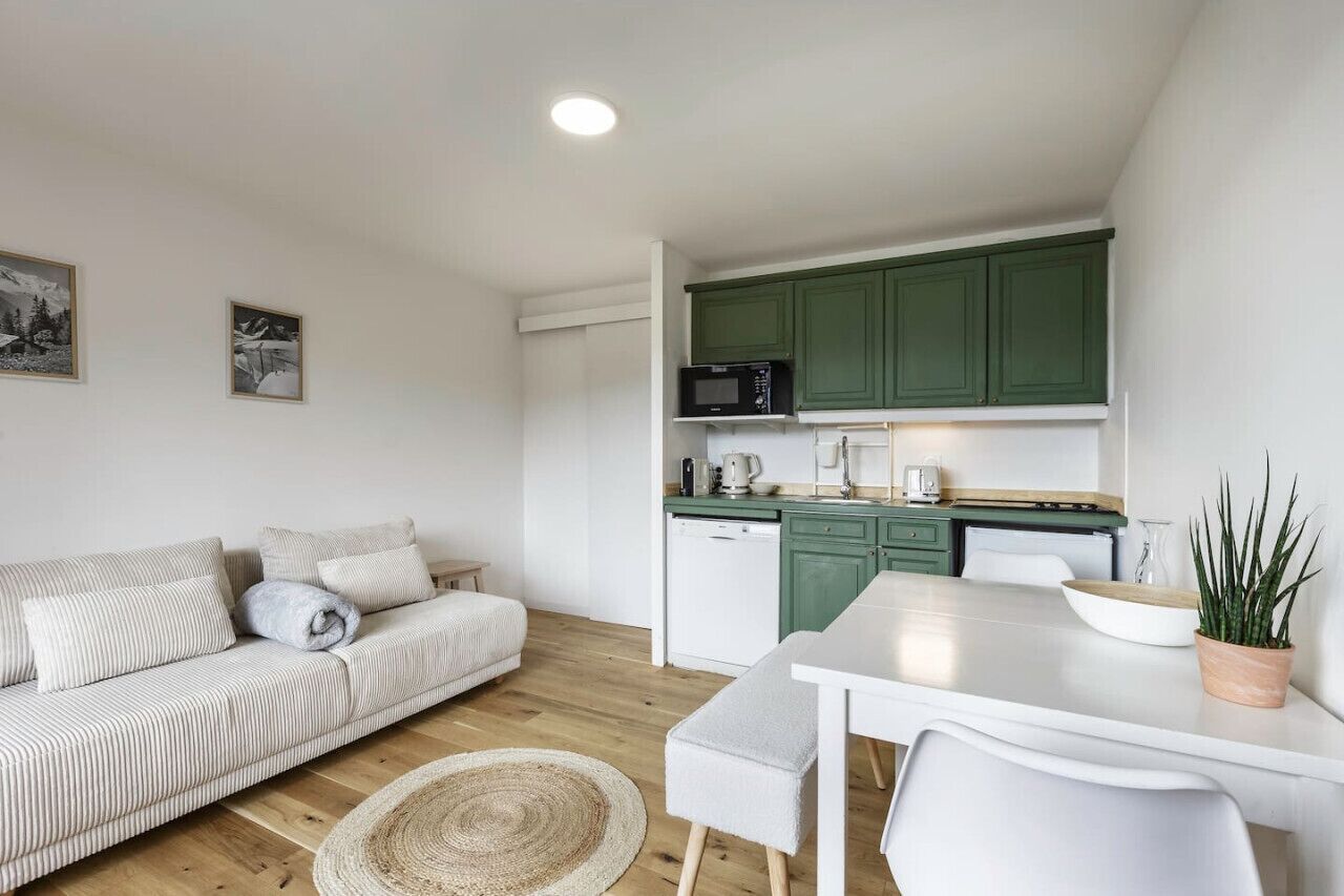 A modern kitchen with green cabinets, a white countertop, and a dining area with a white table and chairs.