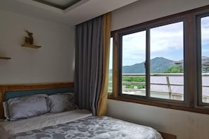 A bedroom with a bed, a window with a view of a mountain and greenery, and a wooden headboard.