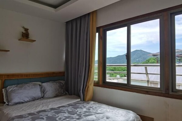 Ein Schlafzimmer mit Bett, Fenster mit Blick auf Berg und Grünfläche, sowie ein Holzkopfteil.