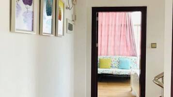 Un pasillo que conduce a un dormitorio con una cama, una cortina rosa y obras de arte enmarcadas en la pared.