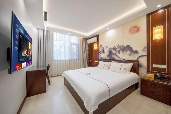 Une chambre d’hôtel avec un grand lit, un téléviseur fixé au mur, une table de chevet en bois et un mur orné d’un tableau représentant une montagne.