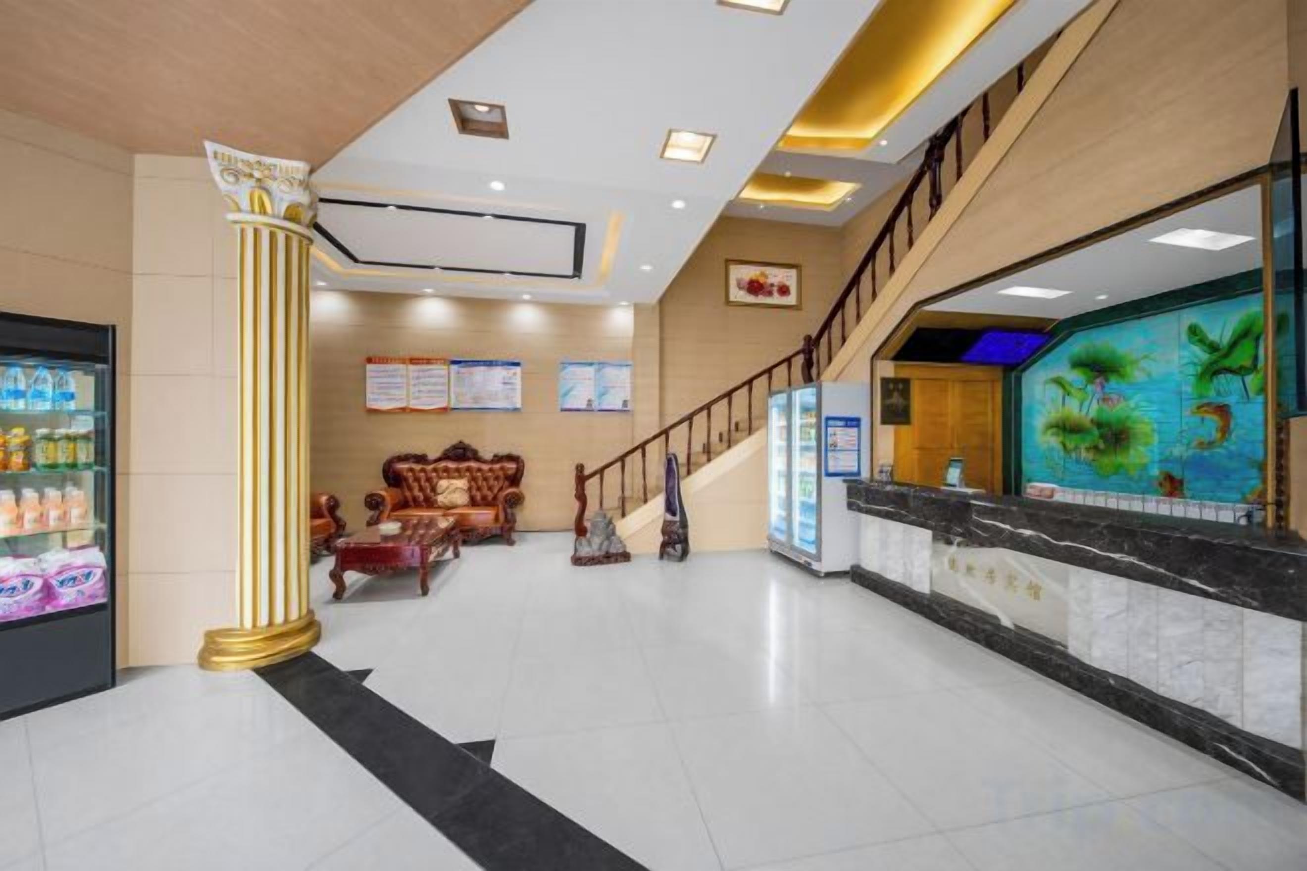 A hotel lobby with a reception desk, a staircase, and a seating area.