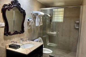 Un baño con lavamanos de mármol, un espejo grande y decorativo, cabina de ducha con mampara de vidrio y un inodoro.