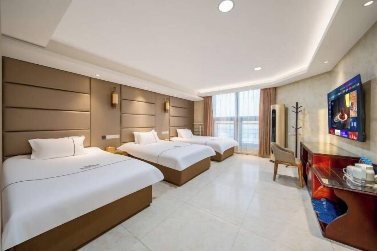 Une chambre d’hôtel avec trois lits, un bureau, une télévision et une grande fenêtre.