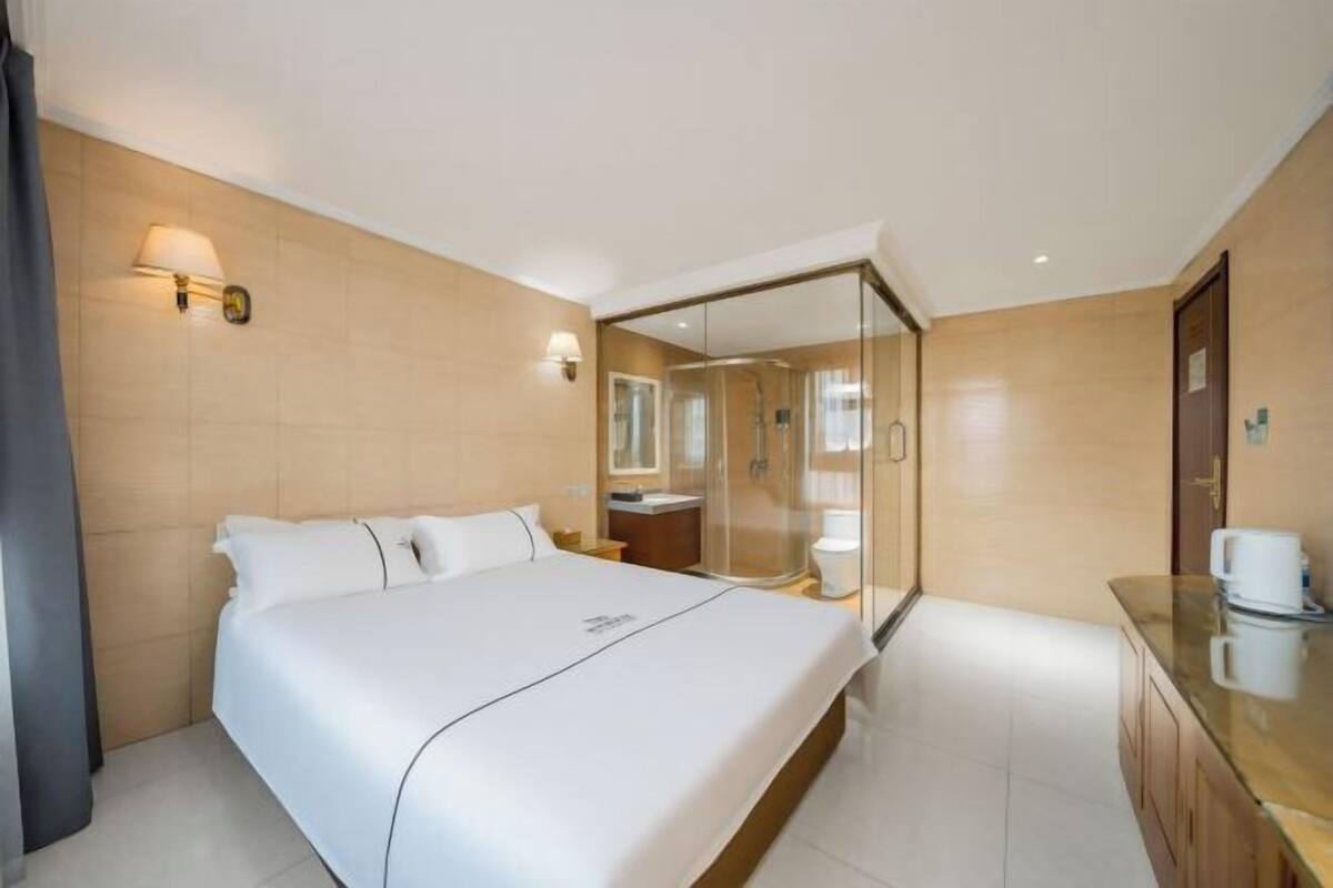 Une chambre d’hôtel avec un grand lit, une douche en verre, une coiffeuse en bois et une petite kitchenette.
