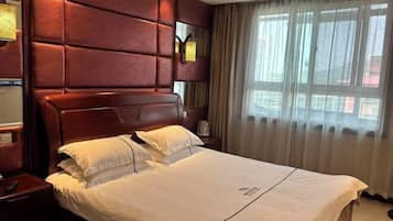 A hotel room with a large bed, a wooden headboard, a nightstand, and a window with curtains.