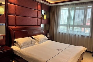 Una habitación de hotel con una cama grande, cabecera de madera, una mesita de noche y una ventana con cortinas.