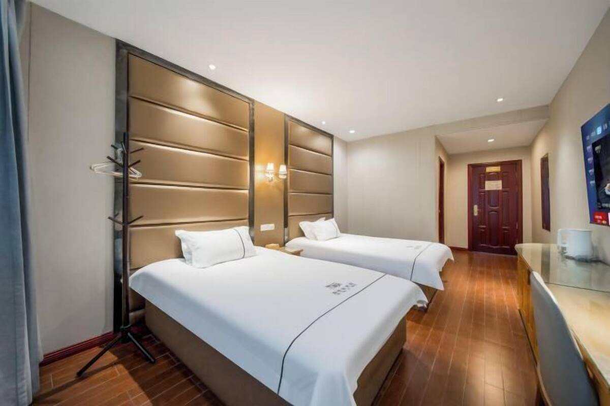 Une chambre d’hôtel avec deux lits, un plancher en bois, un téléviseur posé sur un meuble et une porte visible au fond.