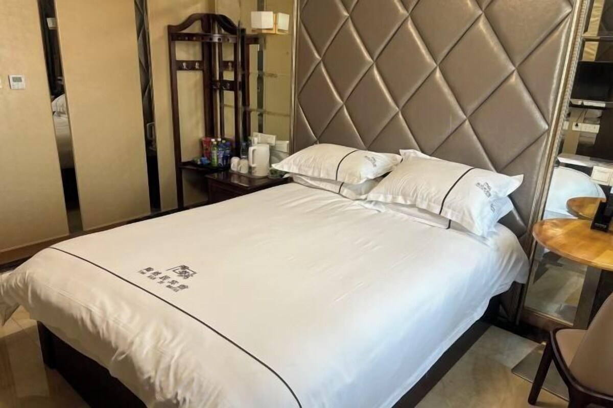 Una habitación de hotel con una cama grande, un cabecero con diseño de rombos, una mesita de noche con lámpara y un espejo.