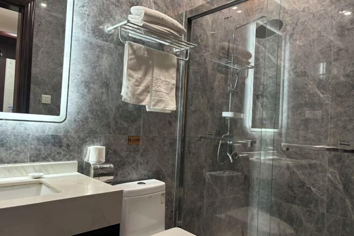 Un baño moderno con ducha envuelta en vidrio, pared de mármol y un perchero.