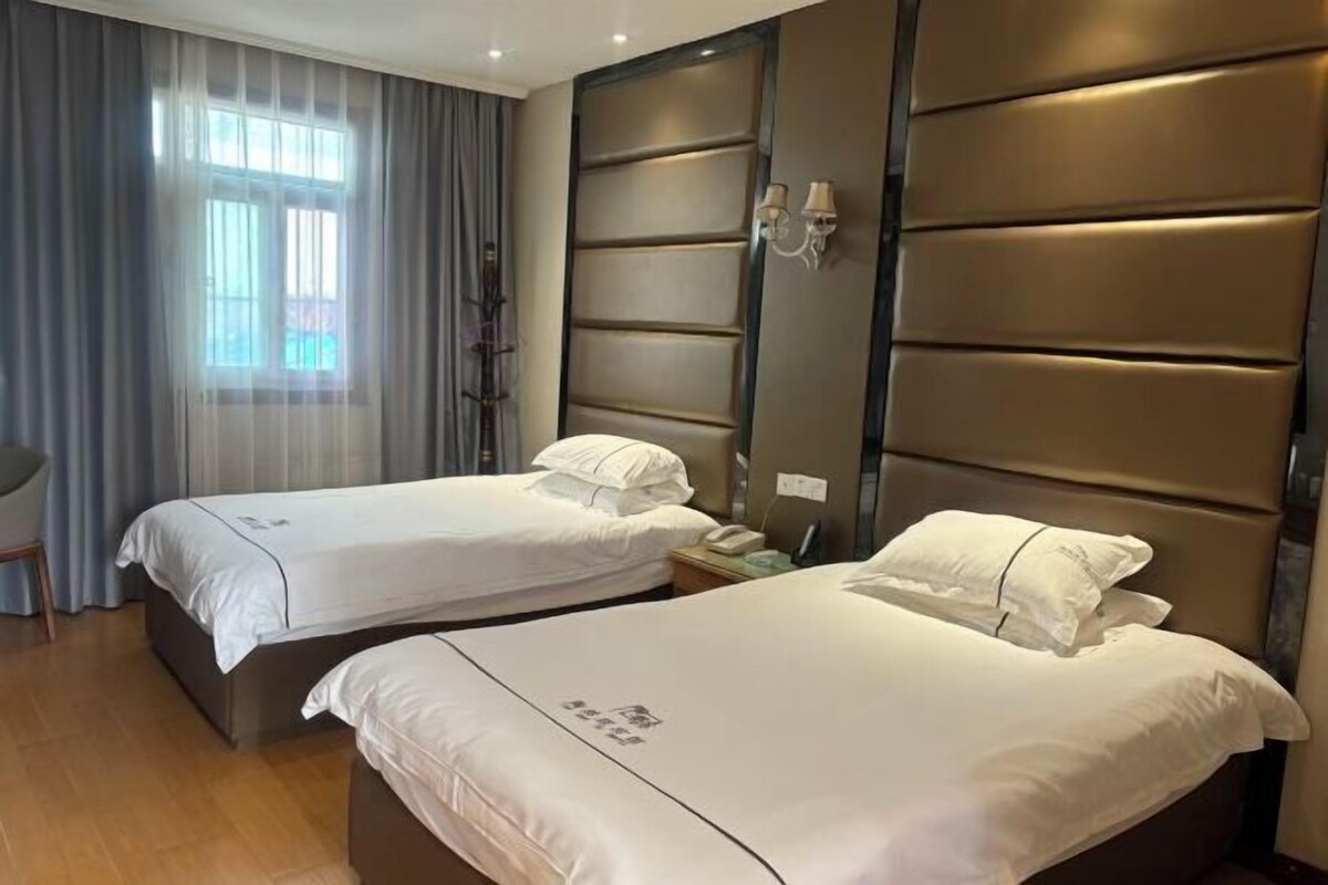 Habitación de hotel con dos camas, un ventanal con cortinas, una lámpara de pared y suelo de madera.