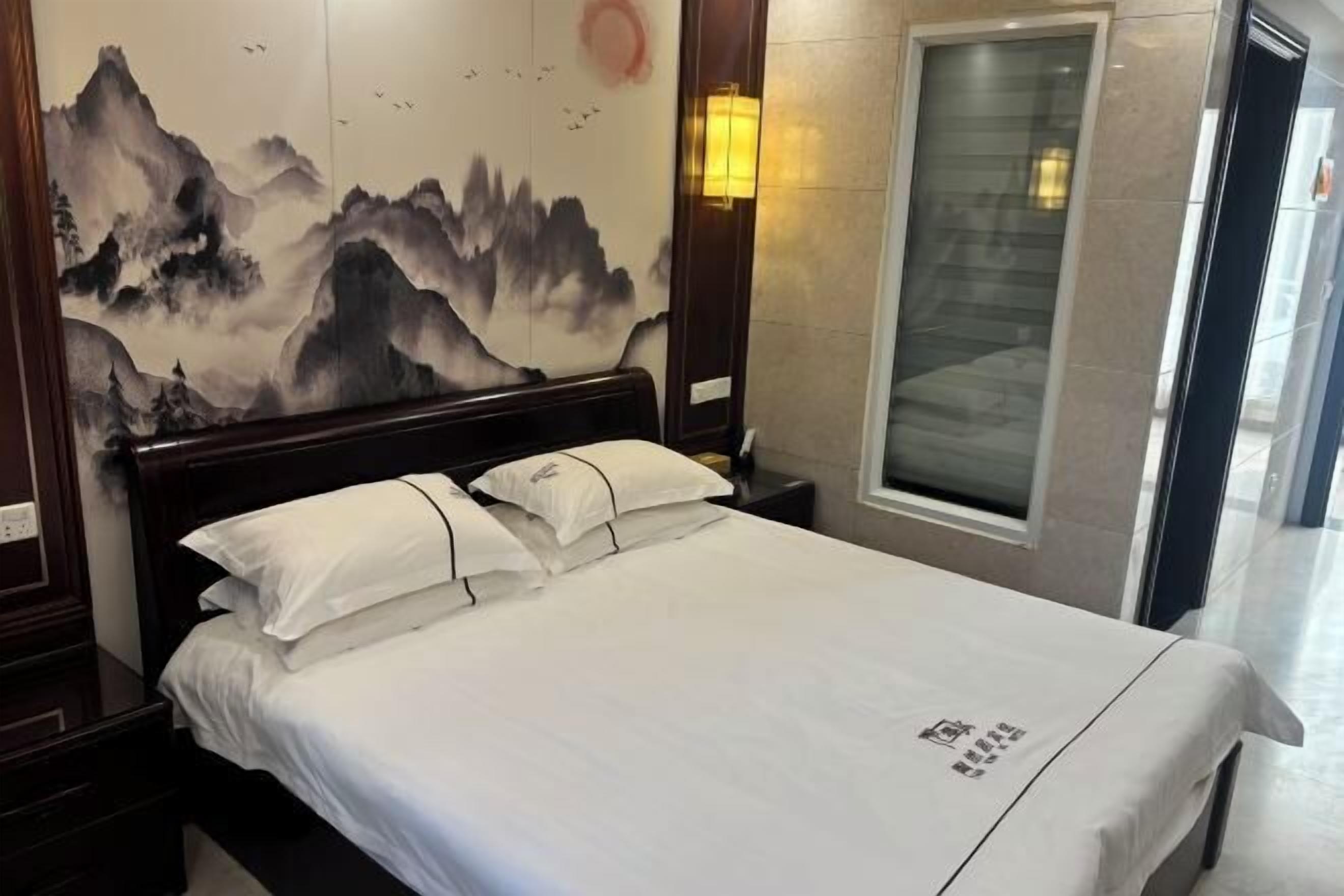 A hotel room with a bed, a wall with a painting, a window, and a door.