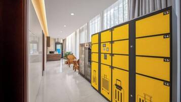 A hotel corridor with lockers numbered 13 to 16, a reception desk, and a seating area with chairs.