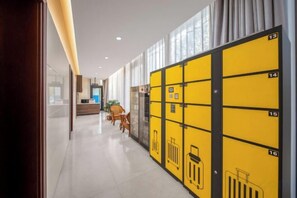 Pasillo de hotel con taquillas numeradas del 13 al 16, un mostrador de recepción y una zona de estar con sillas.