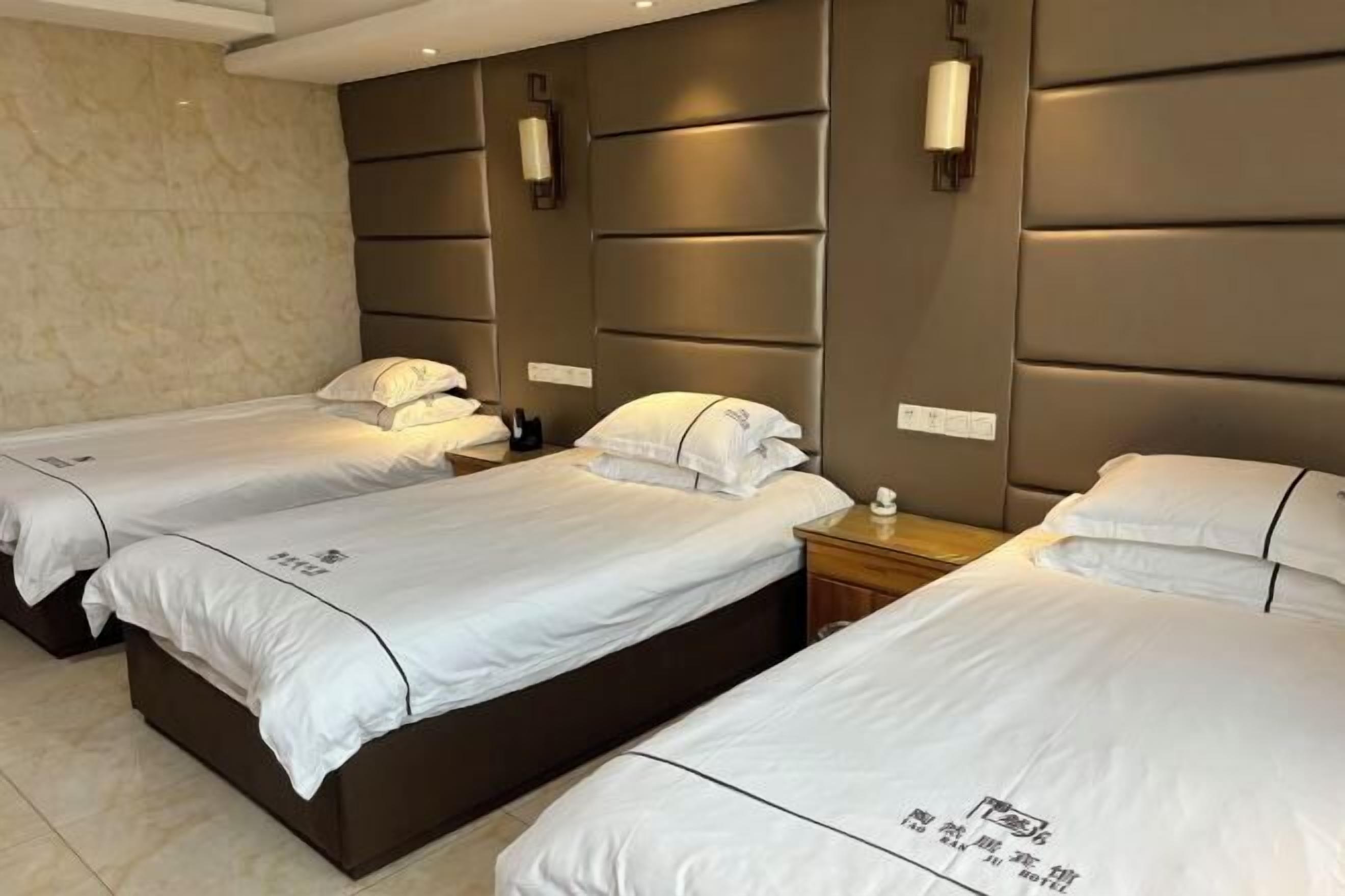 A hotel room with three beds, each with white bedding and pillows, and a headboard with built-in lighting.