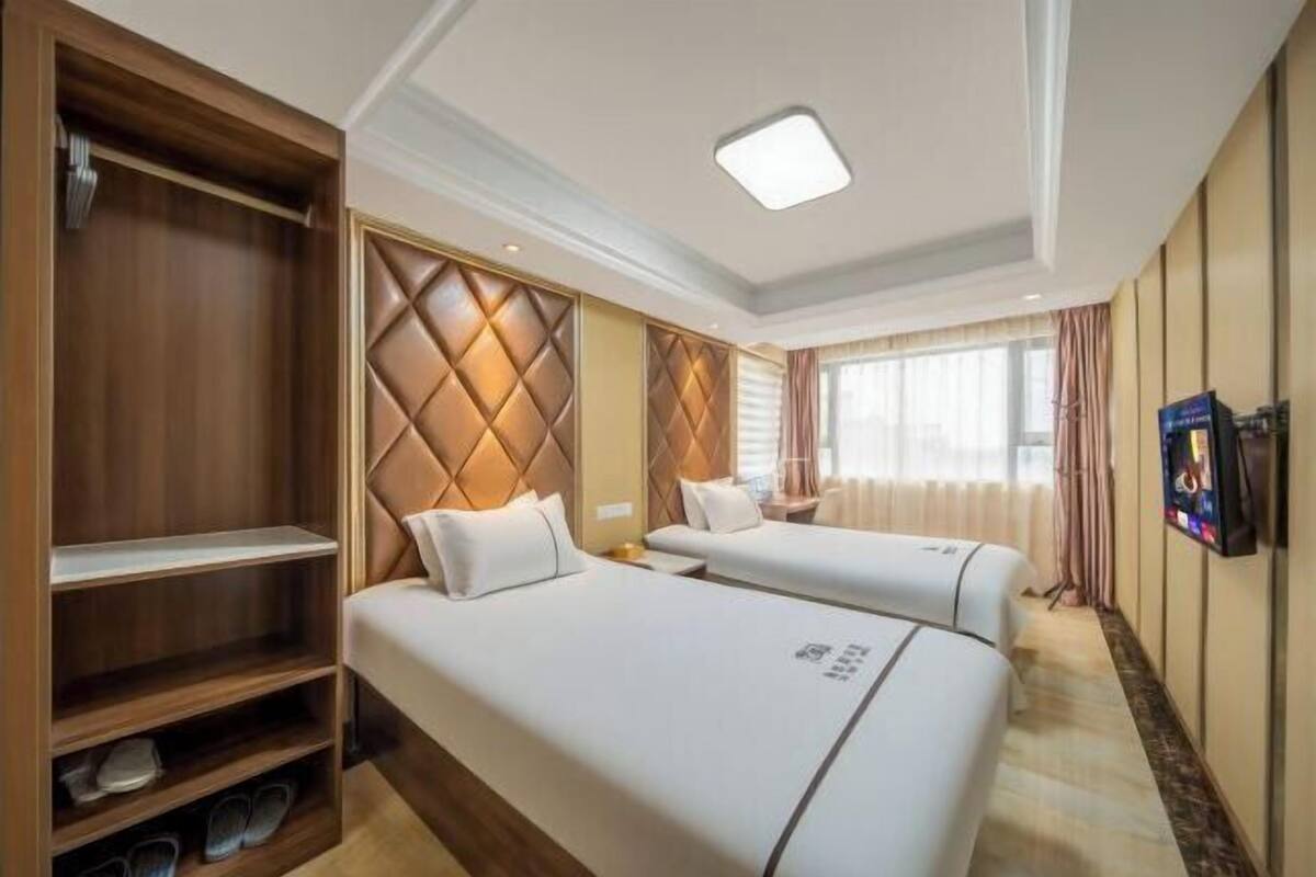 Une chambre d’hôtel avec deux lits, une armoire, une télévision et une fenêtre avec des rideaux.