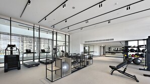 Uma academia moderna com equipamentos de cardio, estações de musculação e amplas janelas com vista para a cidade.