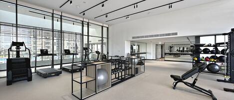 A modern gym with cardio equipment, weightlifting stations, and large windows offering city views.