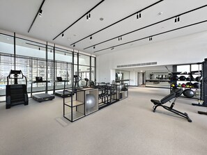 A modern gym with cardio equipment, weightlifting stations, and large windows offering city views.